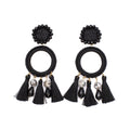 A pair of black bohemian dangle earrings featuring woven circular hoops, hanging black tassels, marbled beads, and faceted black crystal drops on a plain white background.