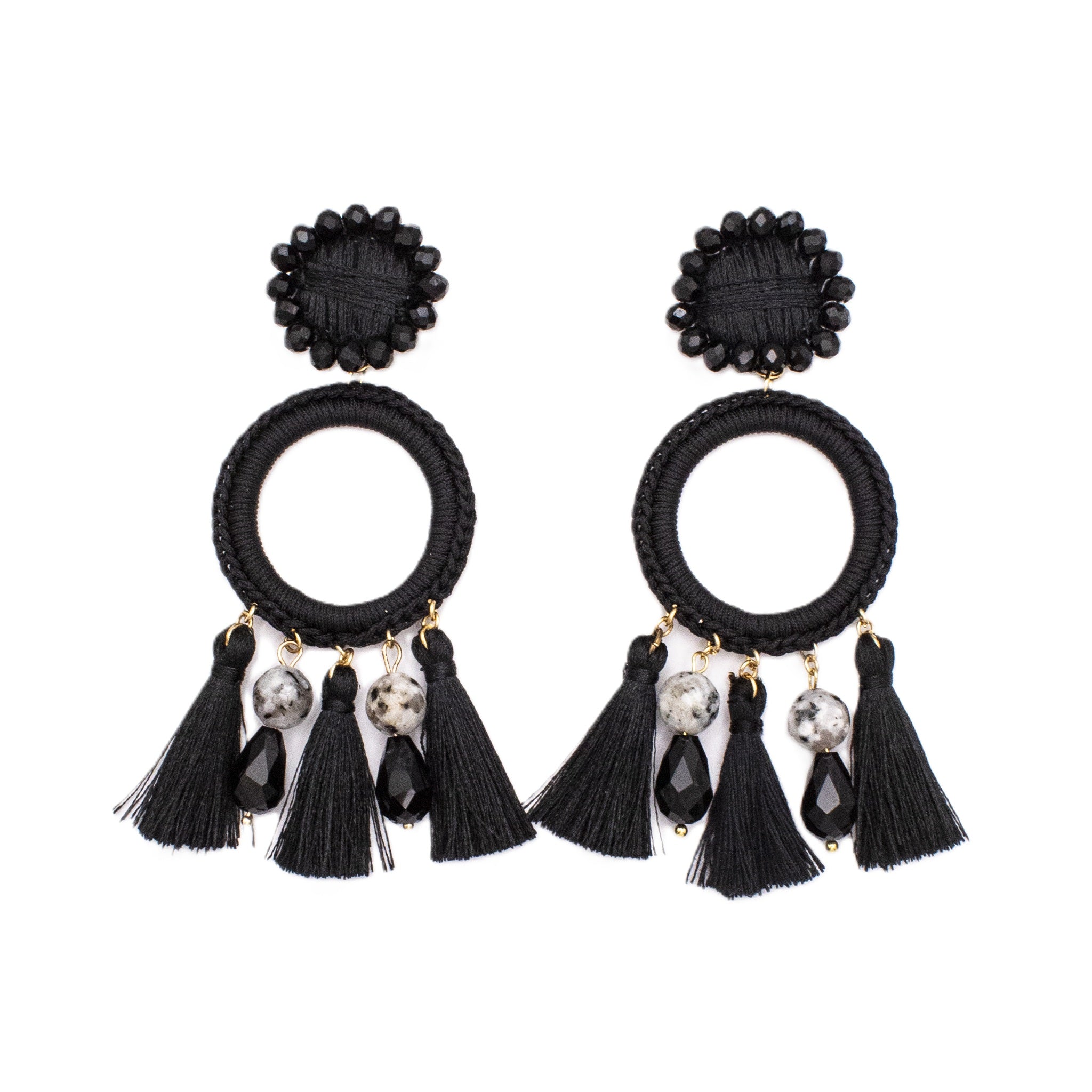 A pair of black bohemian dangle earrings featuring woven circular hoops, hanging black tassels, marbled beads, and faceted black crystal drops on a plain white background.