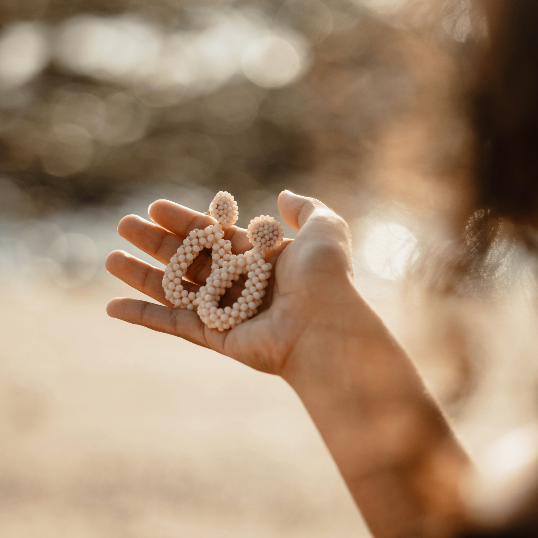 Hand holding a small decorative object against a blurred natural background