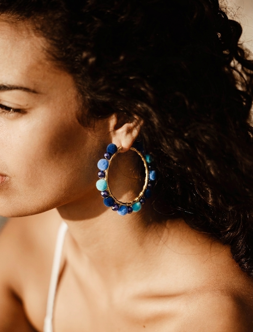 A close-up side profile of a woman wearing a large gold hoop earring adorned with blue and light blue beads.