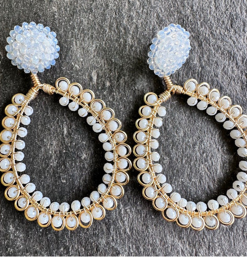Pair of gold hoop earrings with white beads on a dark stone surface