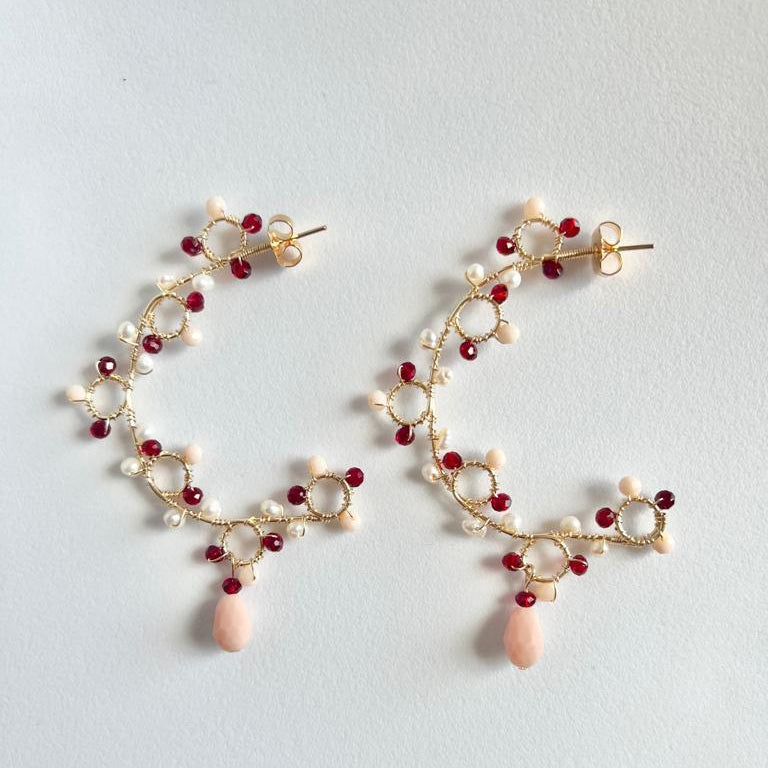 Pair of gold earrings with red and pink beads on a light gray background