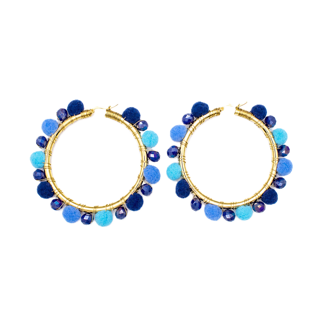 A pair of gold hoop earrings decorated with blue and light blue pom-poms and faceted beads, shown against a plain white background.